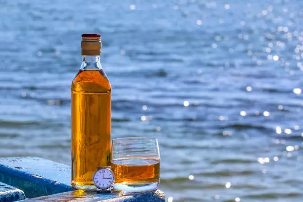 Bottle with glass of the whiskey and the watch on background of the lake