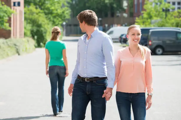 Young Man Walking With His Girlfriend On Street Looking At Another Woman