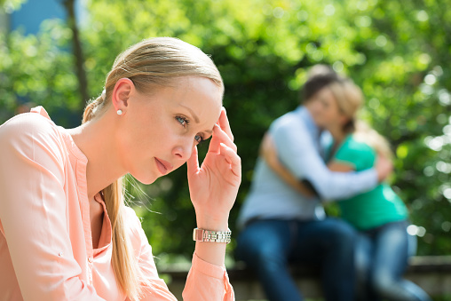 Close-up Of Depressed Young Woman In Front Of Couple Embracing Each Other