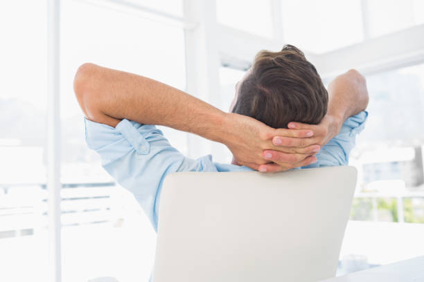 istock Rear view of a casual man resting with hands behind head in office 833529652