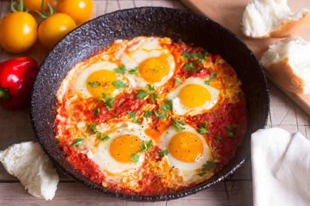 Shakshuka with bread on a wooden table. Middle eastern traditional dish. Homemade. Selective focus. Shakshuka with bread and vegetables on a wooden table. Middle eastern traditional dish. Homemade. Selective focus. libyan culture stock pictures, royalty-free photos & images