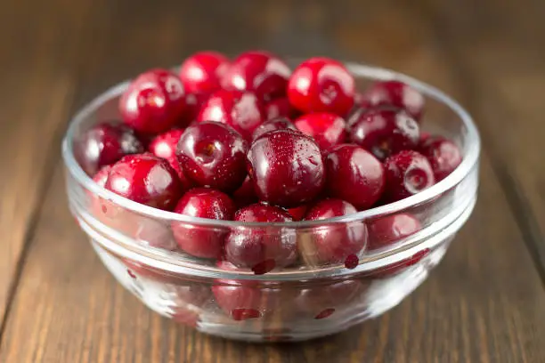 Ripe sweet cherry in the glass bowl on the wooden table. Summer healthy food.