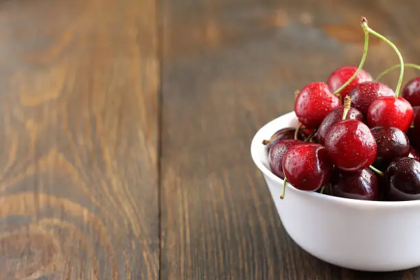 Sweet ripe cherry in white bowl on the table. Tasty summer berries on the wooden background.