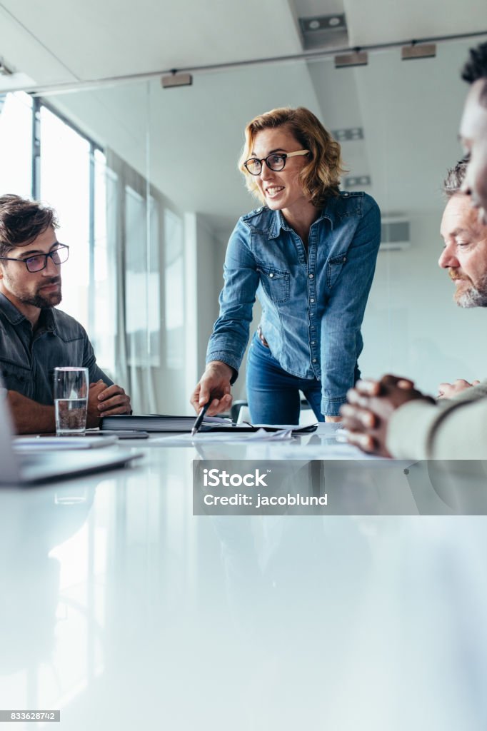 Businesswoman presenting her ideas to coworkers Businesswoman explaining to coworkers about project in office. Beautiful woman explaining her ideas to colleagues in conference room. Meeting Stock Photo