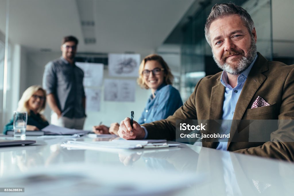 Businesspeople looking at camera with smile Businesspeople looking at camera with smile. Team of designers working in meeting hall. Senior Adult Stock Photo