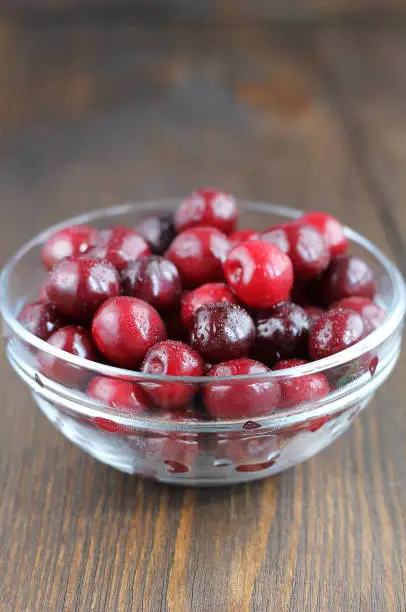 Sweet cherry in glass bowl on the wooden table. Sweet berries covered with drops.
