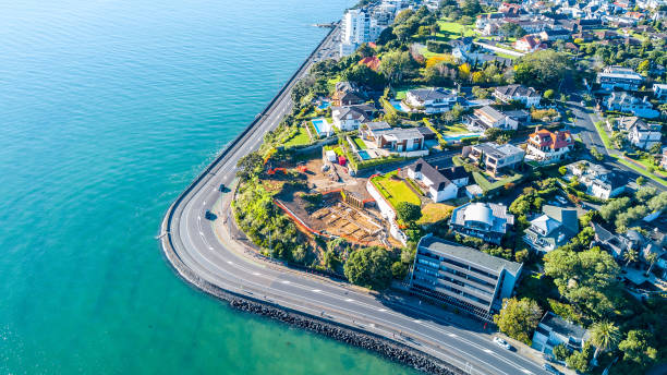 vista aérea em uma estrada, correndo ao longo da costa do mar com subúrbios residenciais no fundo. auckland, nova zelândia. - pacific coast highway - fotografias e filmes do acervo