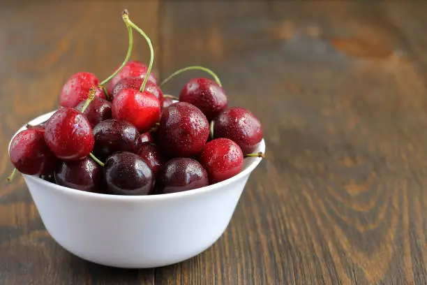 Sweet cherries in bowl on wooden background. Healthy fresh delicious for diet.
