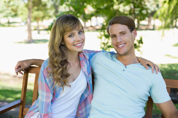istock Cute couple sitting on bench in the park smiling at camera 833646246