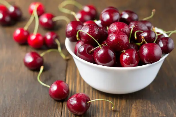 Sweet ripe cherries in white bowl on a table. Beautiful juicy berries on the dark wooden background.