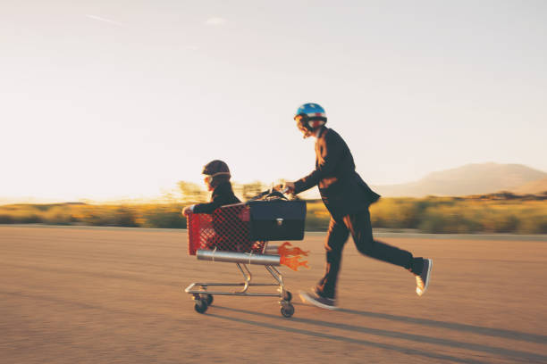 Young Businessmen Racing Rocket Shopping Cart Two young businessmen with helmets, goggles and dressed in business suits run their rocket propelled shopping cart blasting their business to the next level. Both boys are smiling and looking to launch their business profits into the next bracket in Utah, USA. Motion blur. rocketship photos stock pictures, royalty-free photos & images