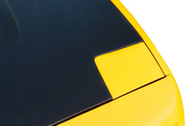 Sports car hood of a yellow and black color isolated against the white background. Play of light and shadows, colors and shapes. Automobile abstract.