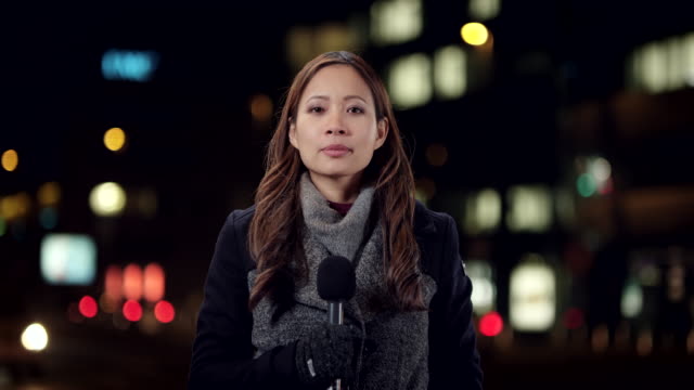 Asian female reporter reporting live from the city center at night