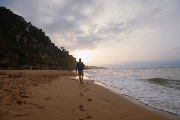 istock Young man walking alone on the beach at sunset, Asturias. 833805222