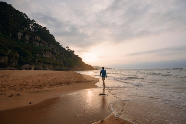 istock Young man walking alone on the beach at sunset, Asturias. 833812640