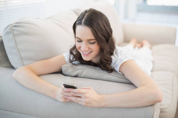 istock Smiling cute woman lying on a cosy couch sending text message 833896918