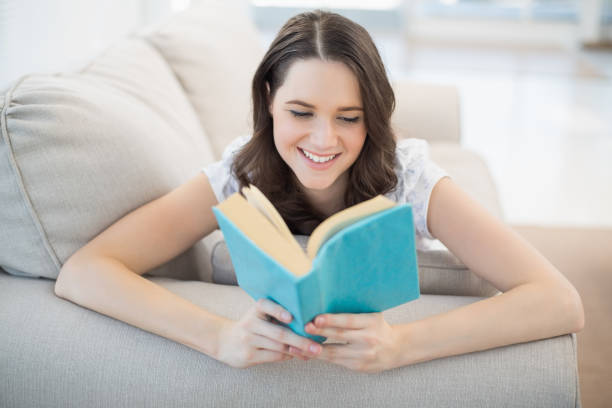 istock Peaceful pretty woman lying on a cosy couch reading book 833897164