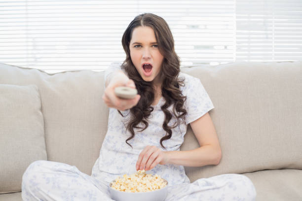 istock Shocked woman in pyjamas having popcorn while watching tv 833975184