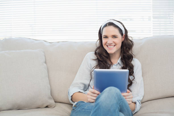 istock Casual woman on cosy couch holding tablet pc 833975776