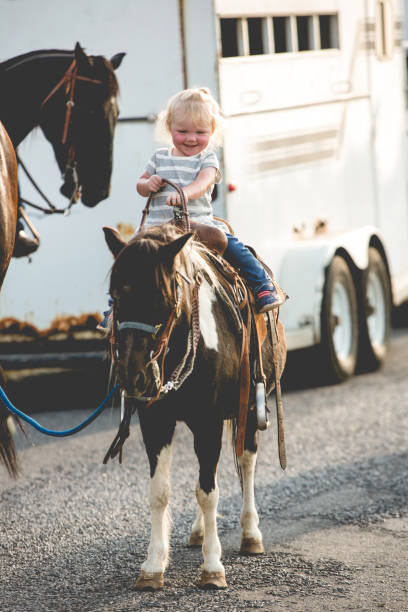 Attractive young man helps his cute toddler daughter riding a horse. equestrian sport for kids, little horseman