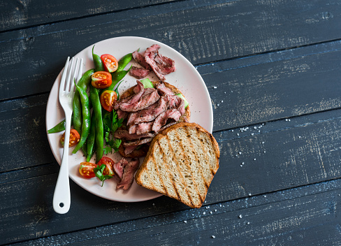 Green beans and grilled steak on toast. Steak sandwich and green beans - healthy snack on a dark background, top view