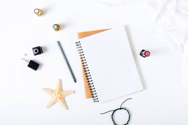 istock Feminine workspace with open notepad, pencil, bracelet and nail polish on white background. Flat lay 834117018