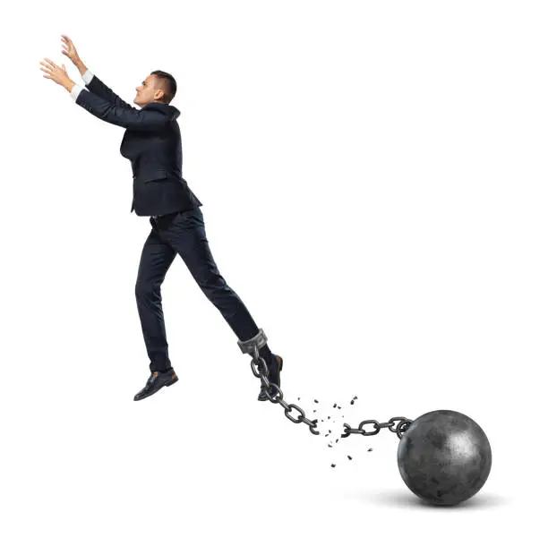 A businessman leaping away from an attached iron ball with a broken chain. Avoiding trouble. Credit refinancing. Business burdens.
