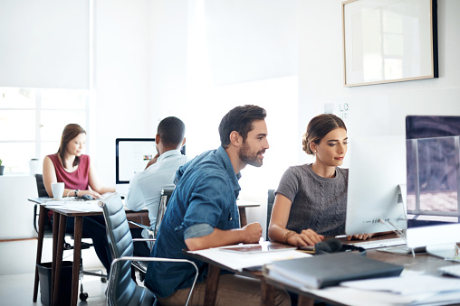 Shot of colleagues using computer together in a modern office