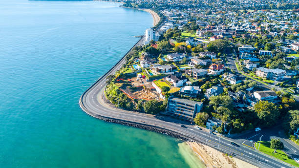 vista aérea em uma estrada, correndo ao longo da costa do mar com subúrbios residenciais no fundo. auckland, nova zelândia. - pacific coast highway - fotografias e filmes do acervo