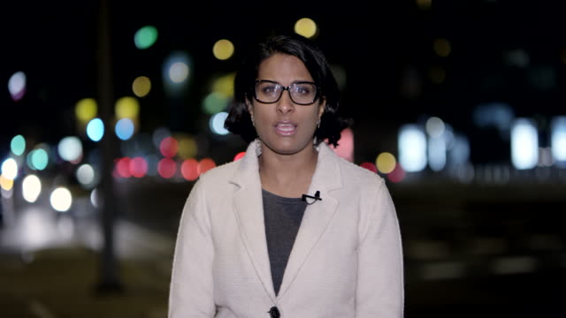 Indian female news reporter reporting live from the city center at night