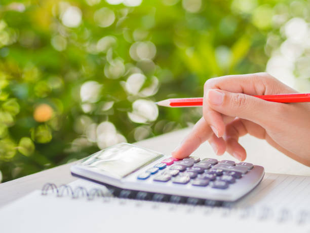 istock woman hand working with calculator and holding red pencil, business document and note book on working table with nature green leaves background. 834213754