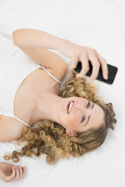 istock Pretty smiling blonde lying on bed holding mobile phone 834251048