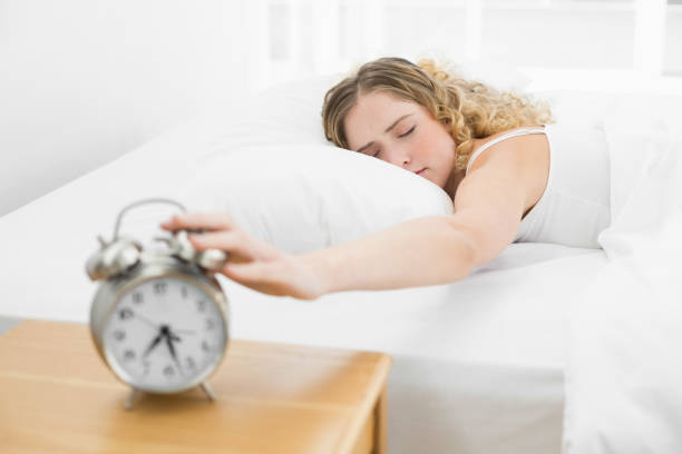 istock Pretty tired blonde lying in bed turning off alarm clock 834251188