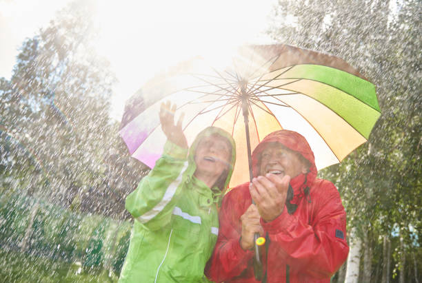 couple marchant dans jour de pluie - umbrella senior adult couple autumn photos et images de collection