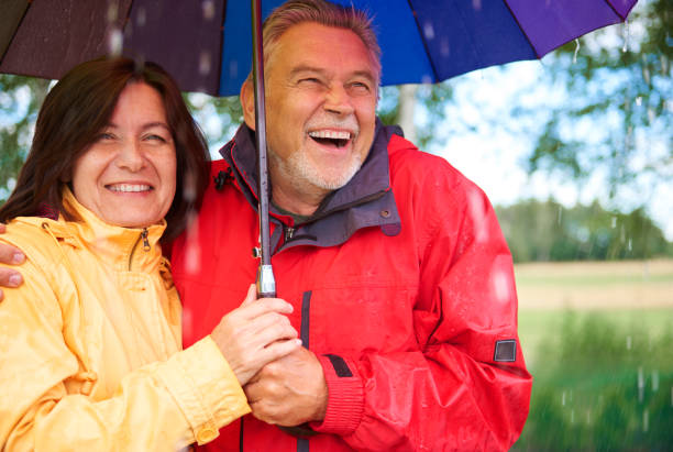 happy senior couple standing during rain - umbrella senior adult couple autumn imagens e fotografias de stock