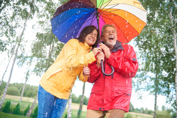 couple humide se cachant sous le parapluie coloré - umbrella senior adult couple autumn photos et images de collection