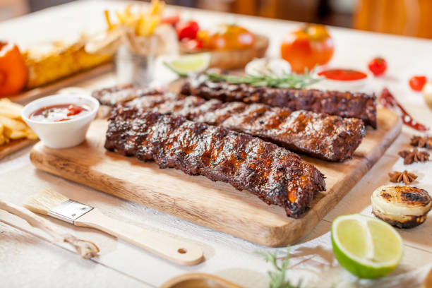 istock Spicy hot grilled spare ribs from a summer BBQ served with chips, corn and fresh tomatoes on an old wooden cutting board 834297622