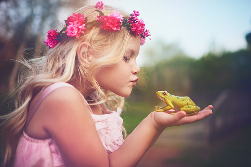 Shot of a cheerful little girl holding a frog and going in for a kiss while standing outside in nature