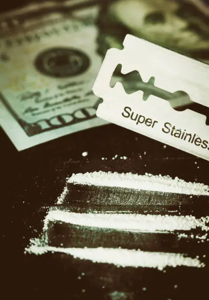 Neatly chopped lines of cocaine or methamphetamine, plus a razor blade, sit next to an American Hundred Dollar banknote.