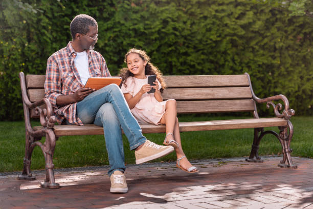 istock girl and her grandfather using smartphone and digital tablet while sitting on bench 834343978