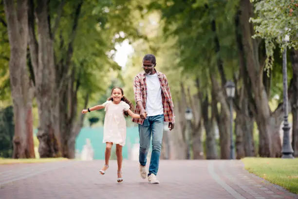 Photo of granddaughter holding hands with grandfather and walking in park