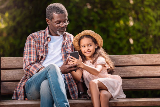 istock girl and her grandfather using smartphone sitting on bench together 834350056