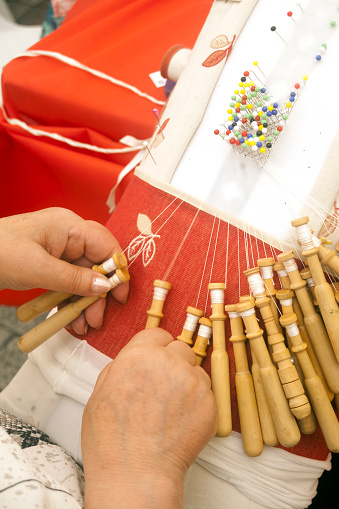 Manufacturing complex bobbin lace , senior woman's hands working. High angle vertical view. Defocused design.