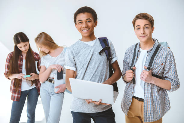 adolescente americano africano segurando laptop enquanto amigos perto aguardando isolaram no branco - telephone child isolated on white elegance - fotografias e filmes do acervo
