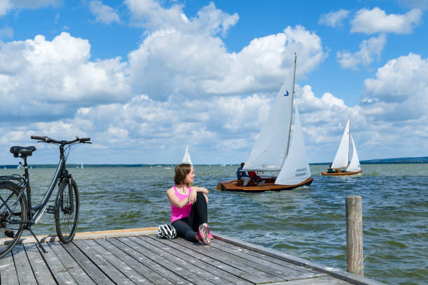 donna con bicicletta seduta sul molo per rilassarsi guardando le barche a vela sul lago - steinhuder meer foto e immagini stock