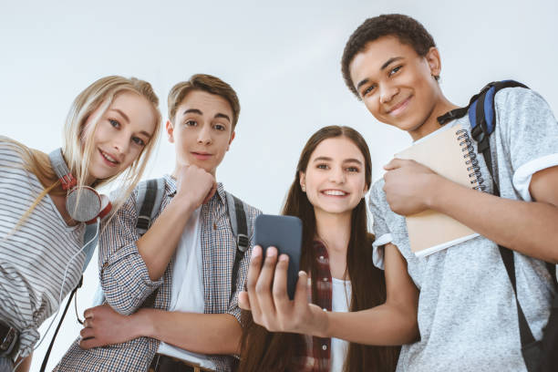 niedrigen winkel ansicht der multikulturellen lächelnde teenager mit smartphone zusammen isoliert auf weiss - telephone child isolated on white elegance stock-fotos und bilder
