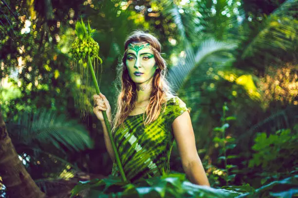 Beautiful woman with creative green makeup, blending in with the jungle.