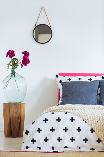 White wall, round mirror, glass vase and patterned bedclothes
