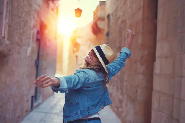Happy woman in hat dancing on mediterreanen street in sunset