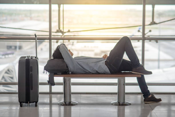 young asian man avec bagages valise et sac à dos, couché sur le banc au terminal de l’aéroport - lying in wait photos et images de collection